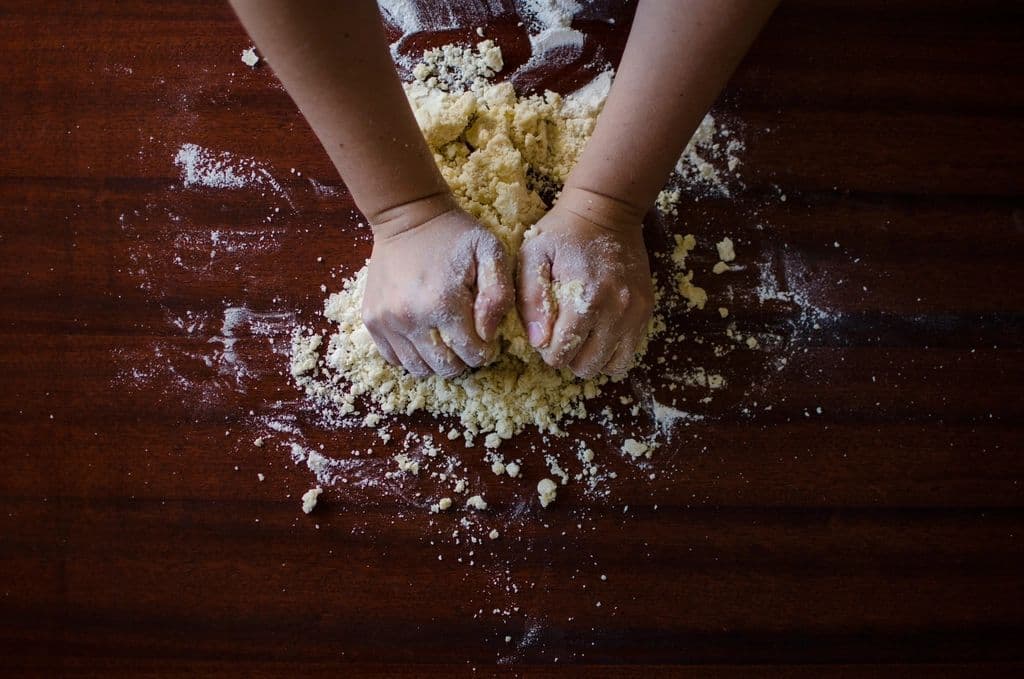 Mani che lavorano farina e acqua sul banco