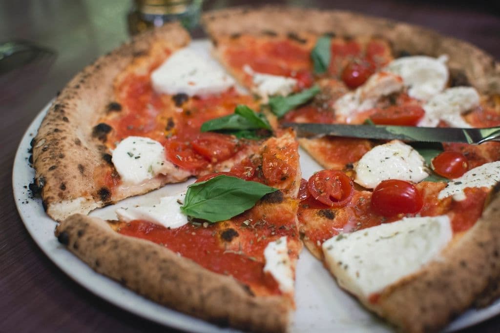 Pizza con mozzarella, pomodorini e basilico, tagliata a spicchi