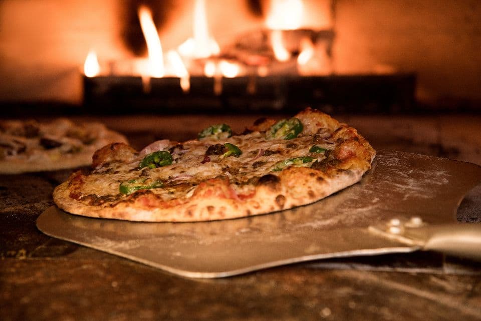 Una pizza sulla pala davanti alla fiamma del forno